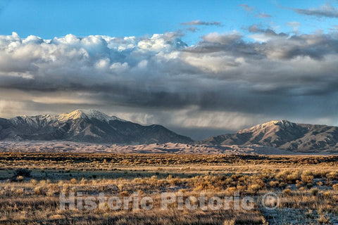 Photo- Distant view of Great Sand Dunes National Park & Preserve (the brownish hills of sand below the Sangre de Cristo Mountain Range) in south-central Colorado's Alamosa County